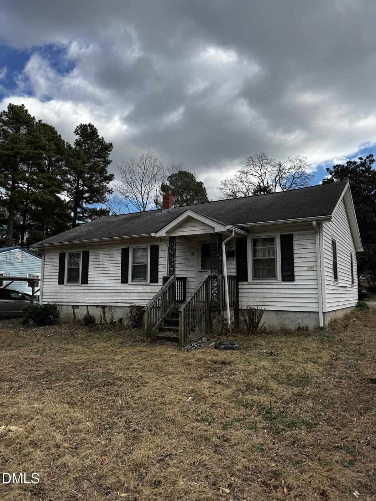 A small white house with black shutters and a front porch sits on a patchy, brown lawn under a cloudy sky at 819 Arrow Street in Henderson. Tall trees are visible in the background.