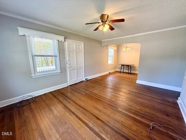 A bright living room with hardwood floors, a ceiling fan, and two windows. An arched doorway leads to a dining area with a hanging light and a small table. Walls are painted light gray.