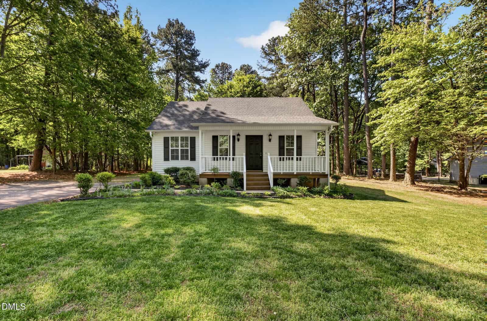 A small white house at 137 Bridges Lane, Youngsville, with a front porch, black door, and steps leading up. It sits on a well-maintained green lawn, surrounded by trees and shrubs, with a driveway and forested area in the background.