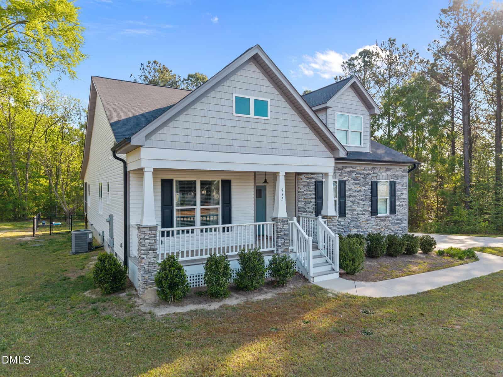 A modern two-story house at 952 Brantleytown Road, Zebulon, with light-colored siding, stone accents, a covered front porch, white railings, and neatly trimmed bushes on a spacious lawn under a clear blue sky.