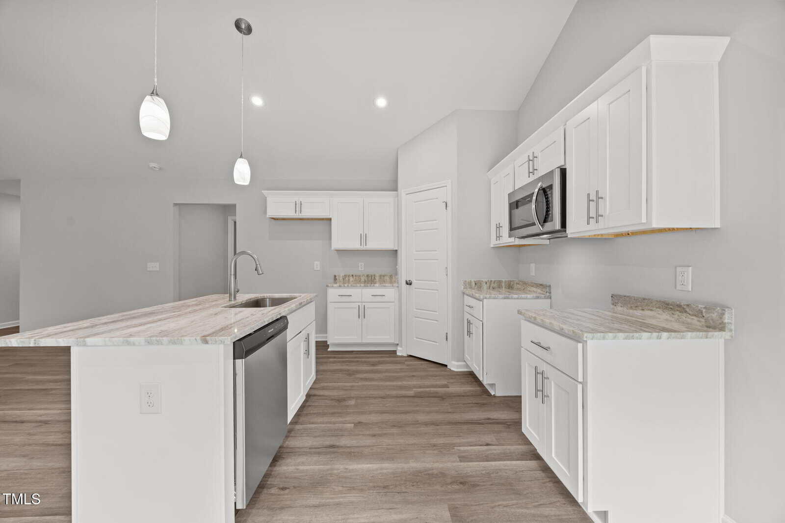 Modern kitchen with white cabinets, stainless steel appliances, marble countertops, pendant lights, wood-style flooring, and neutral walls, creating a bright and spacious atmosphere.