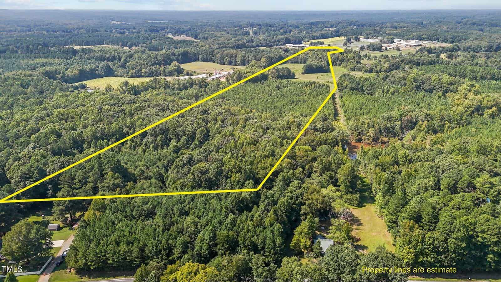 Aerial view of a large, forested area with a yellow outline indicating property boundaries. The land is densely wooded, surrounded by more trees, roads, and some scattered buildings in the distance.