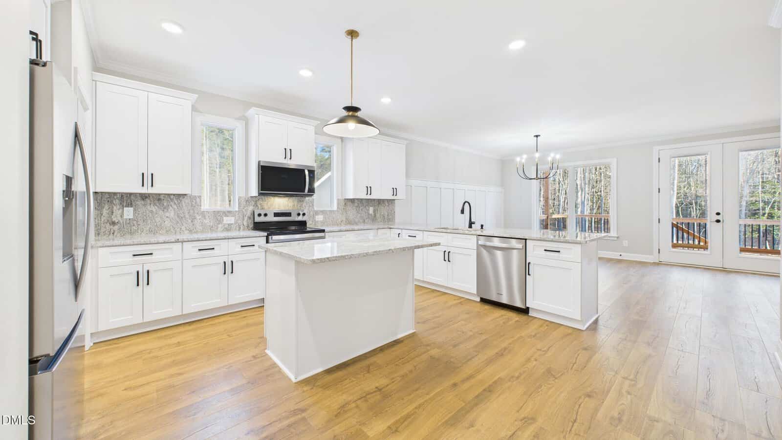 Bright, modern kitchen with white cabinets, a central island, stainless steel appliances, granite countertops, wood flooring, and large windows and doors letting in natural light and offering a view of trees outside.