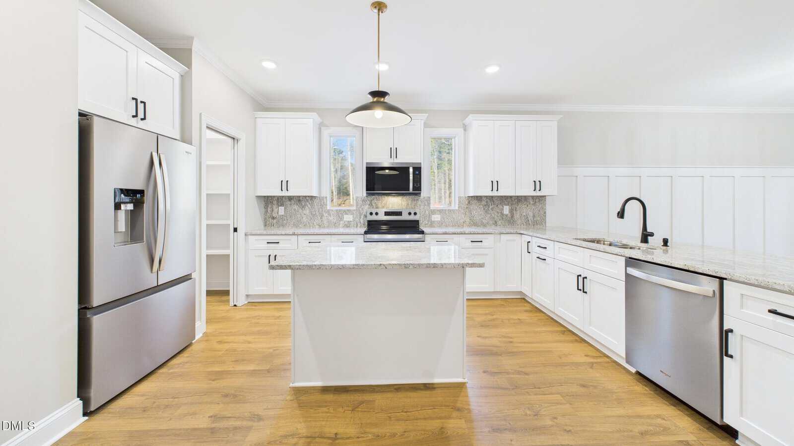 Bright modern kitchen with white cabinets, stainless steel appliances, a central island with granite countertop, wood flooring, and two windows above the stove letting in natural light.