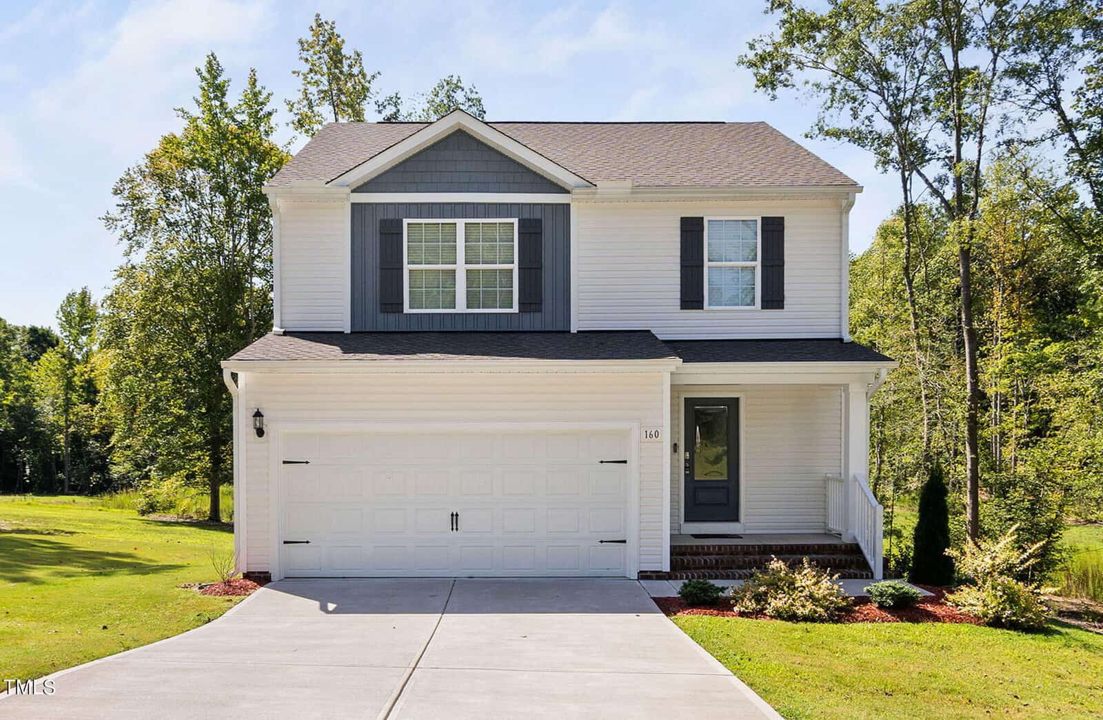A modern two-story house with white siding, dark gray shutters, a double garage, and a covered front porch. The home sits on a manicured lawn with trees and bushes in the background under a clear sky.