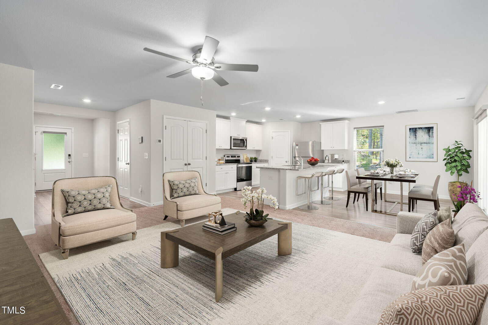 Bright, open living area with a beige sofa, two armchairs, coffee table, modern kitchen, dining table, and large windows. Light decor with plants and neutral tones throughout.