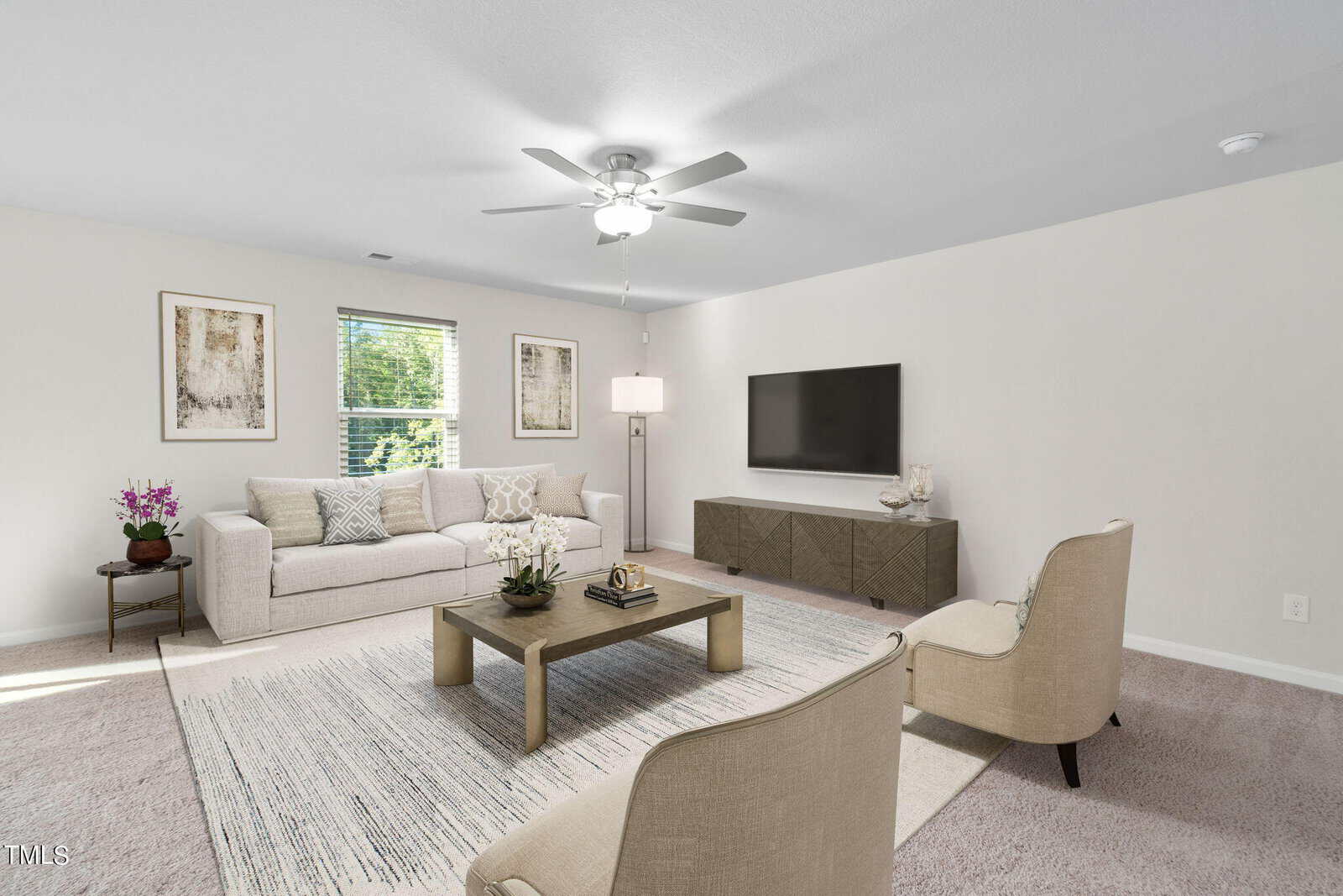 Modern living room with beige walls, a white ceiling fan, neutral sofa, two armchairs, a coffee table, a TV on a console, and wall art. Natural light comes from a window beside the sofa.