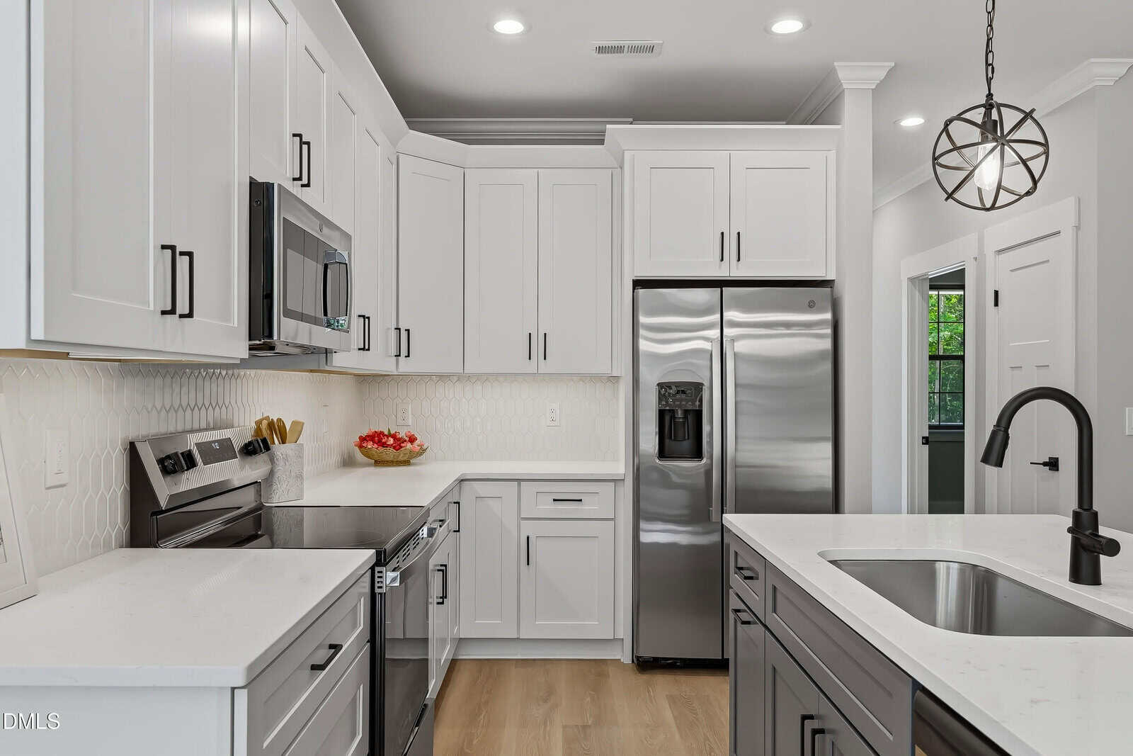 Modern kitchen with white cabinets, stainless steel appliances, a large fridge, built-in microwave, electric stove, and an island with a sink and dark faucet. Light wood floors and bright lighting complete the clean, contemporary design.