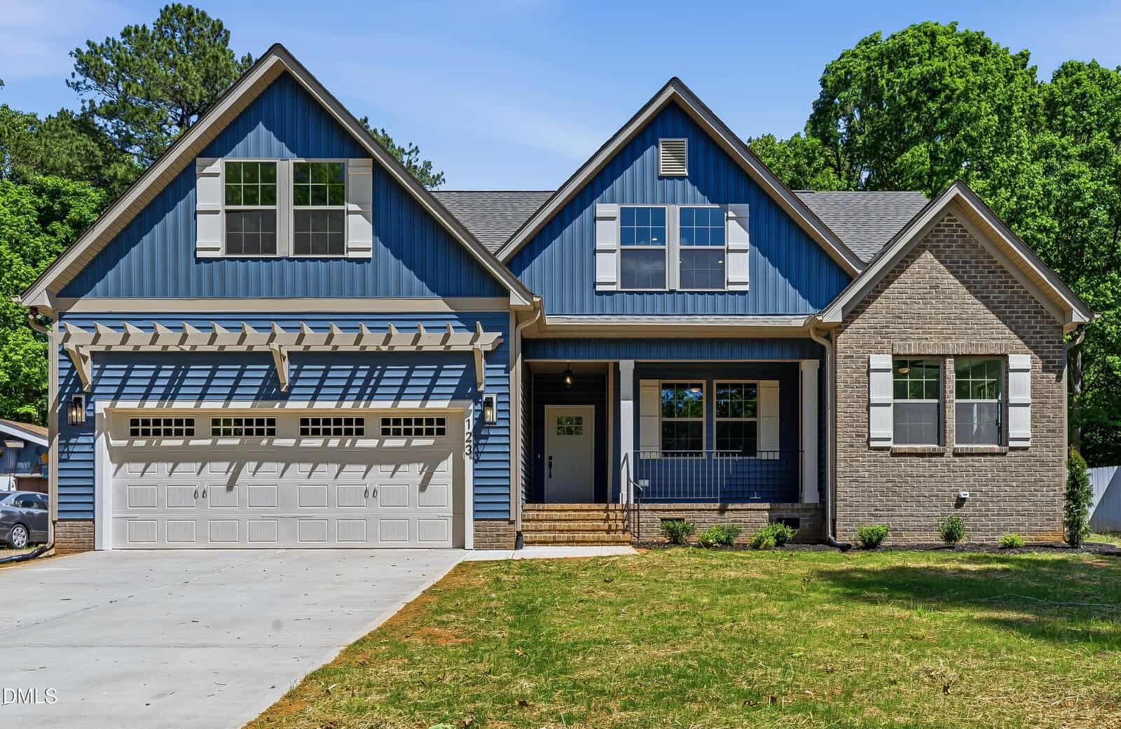 A modern suburban house with blue siding and brick accents, featuring a two-car garage, large front porch, multiple windows with white trim, and a well-maintained lawn under a clear blue sky.