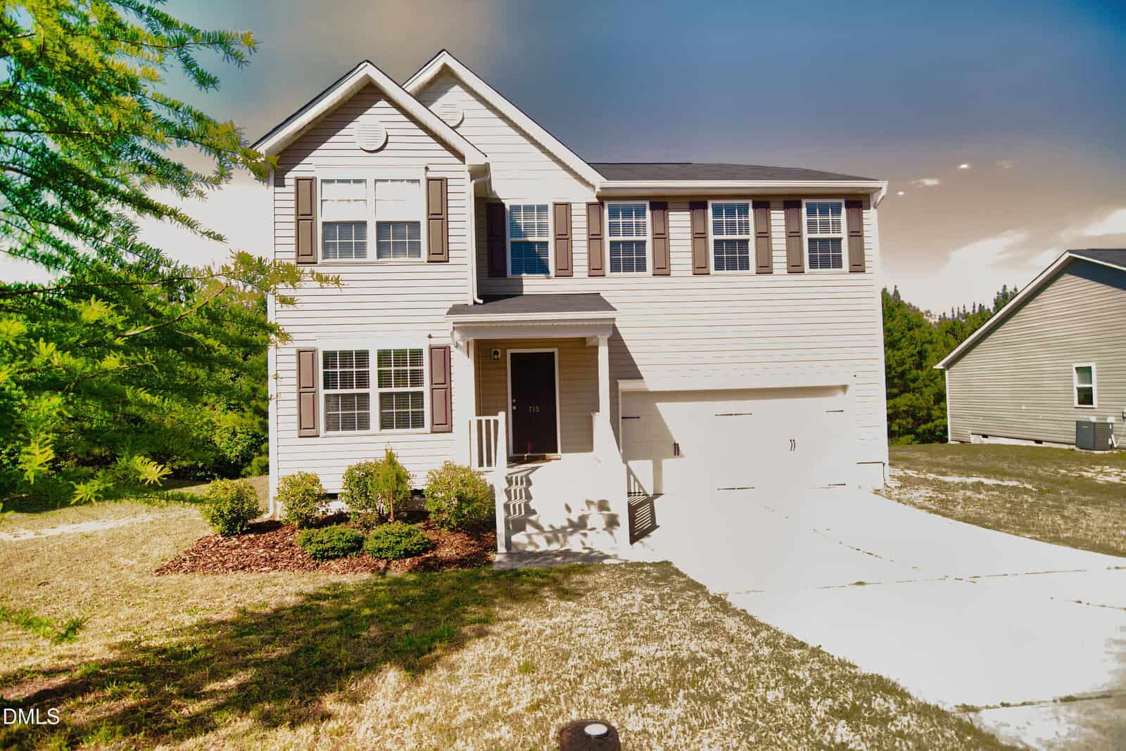 Two-story beige house with dark shutters, a black front door, attached garage, small front porch, landscaped bushes, and a curved driveway. The sky is partly cloudy with a gradient effect.