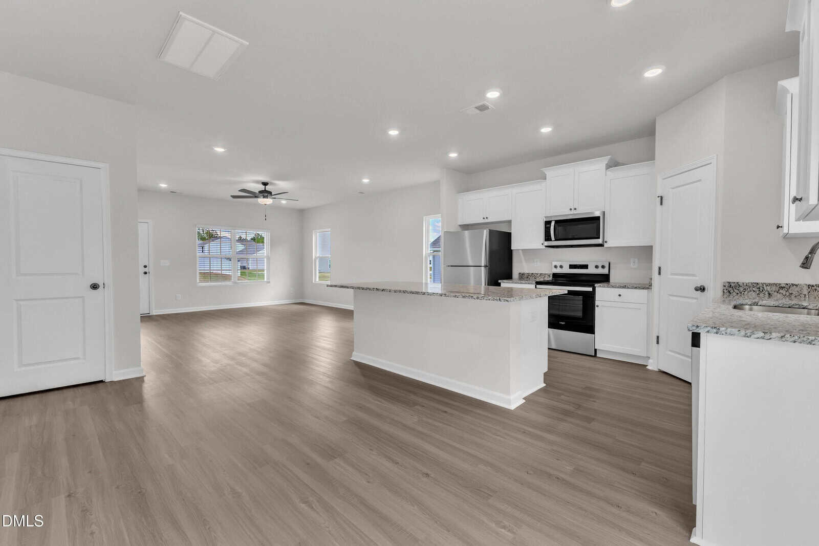 Modern open-concept kitchen and living area with white cabinets, stainless steel appliances, a center island, wood-style flooring, recessed lighting, and large windows letting in natural light.