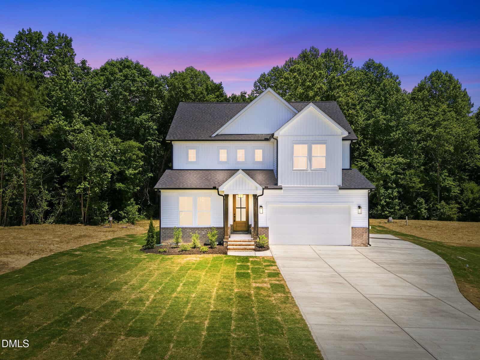 A two-story modern house with white siding at 75 Basil Court, Franklinton, features a front porch and double garage, set on a large, neatly manicured lawn with a wooded area in the background at sunset.