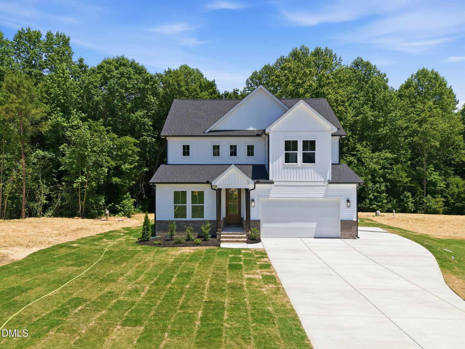 A modern two-story white house with dark roof and trim, double garage, and neatly landscaped front yard. The home is surrounded by trees and has a fresh green lawn with a curved driveway.