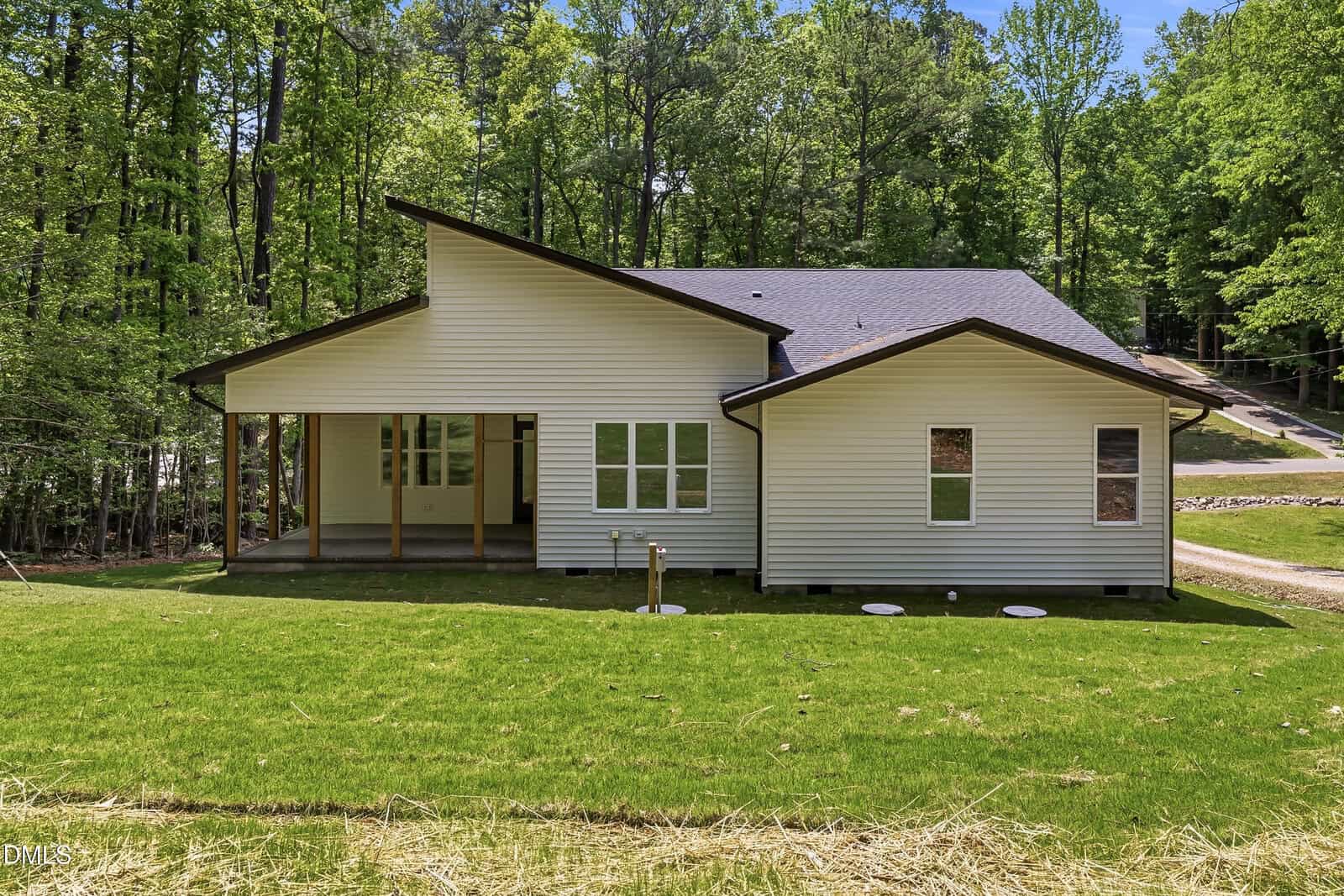 A modern single-story white house with a sloped roof, large windows, and a covered porch, surrounded by green grass and trees under a sunny sky.