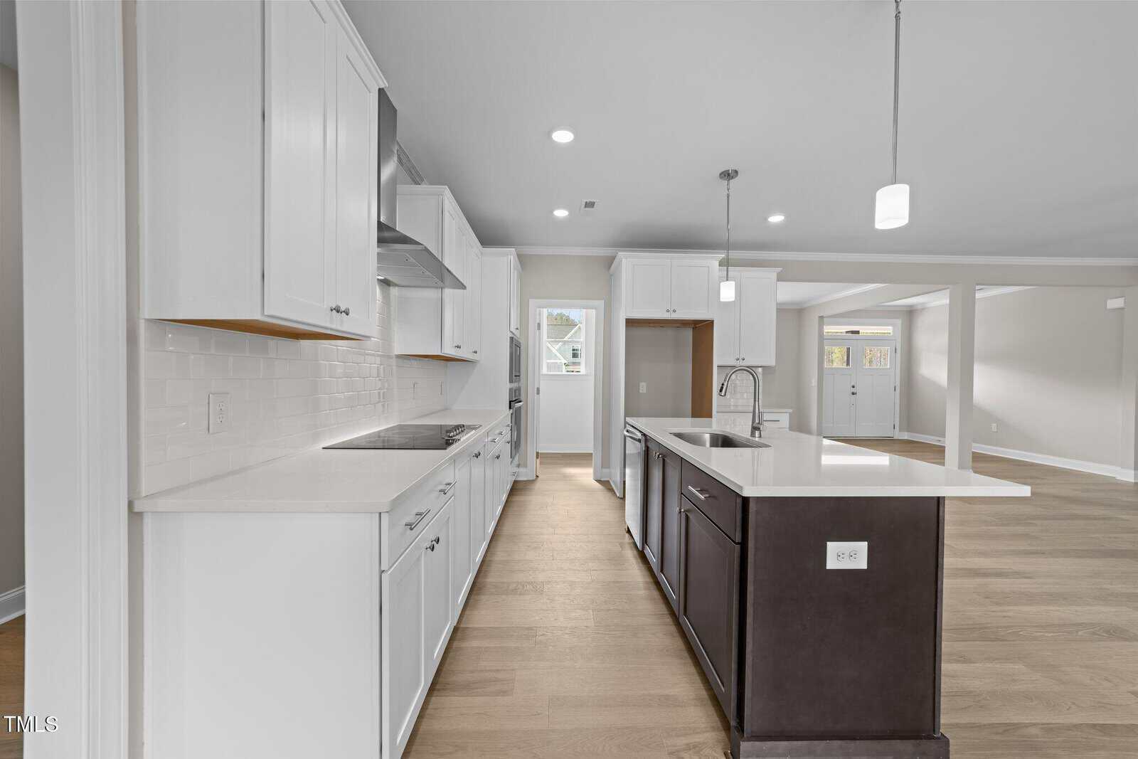 Modern kitchen with white cabinets, a dark island with a sink, light wood floors, white subway tile backsplash, and stainless steel appliances. Open layout connects to living and dining area with large windows.
