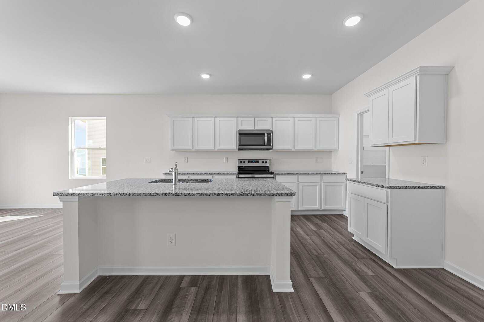 Modern kitchen with white cabinets, granite countertops, stainless steel appliances, and dark wood flooring. The space is well-lit with recessed lighting and natural light from a window on the left.