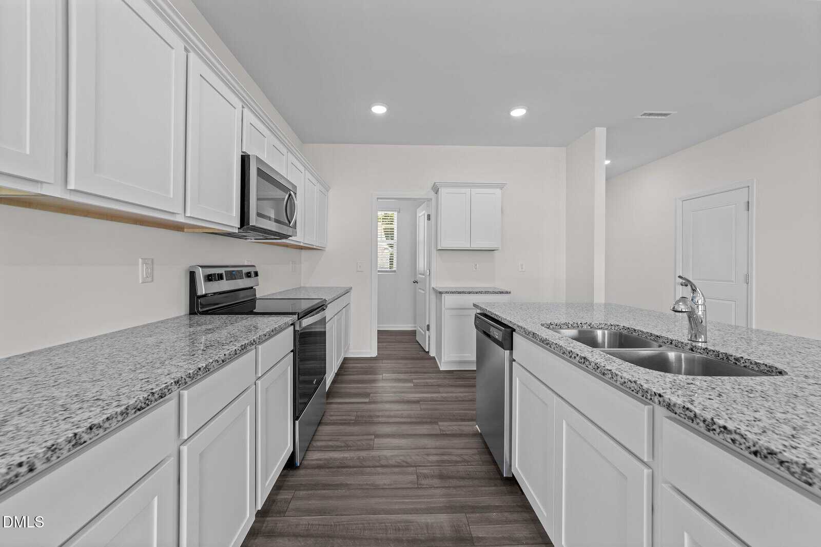 Modern kitchen with white cabinets, granite countertops, stainless steel appliances, a double sink on the island, and dark wood flooring. The space is well-lit with recessed ceiling lights.