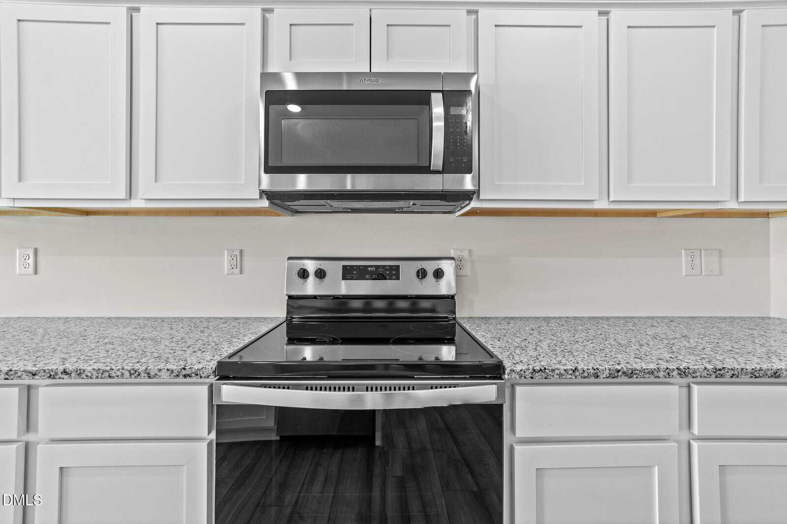 Modern kitchen with white cabinets, granite countertops, a stainless steel electric stove, and a microwave oven mounted above the stove. The flooring is dark wood.