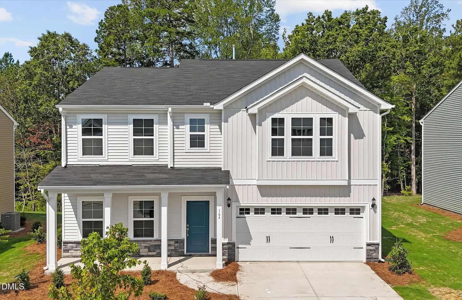 Two-story suburban house with white siding, dark roof, blue front door, double garage, and front porch at 164 Sugarmaple Way in Youngsville. Well-kept lawn and trees in the background under a sunny sky.