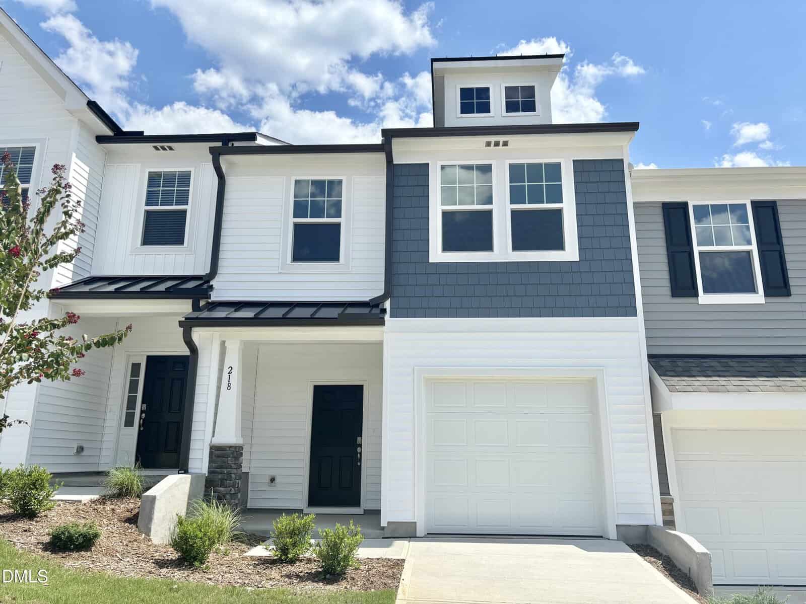 A two-story townhouse with white and gray siding, black door, attached single-car garage, small front yard, and a concrete driveway under a partly cloudy sky. Located in Franklinton, the house number 216 is visible beside the front door, just down the street from 218 Alberta Drive.