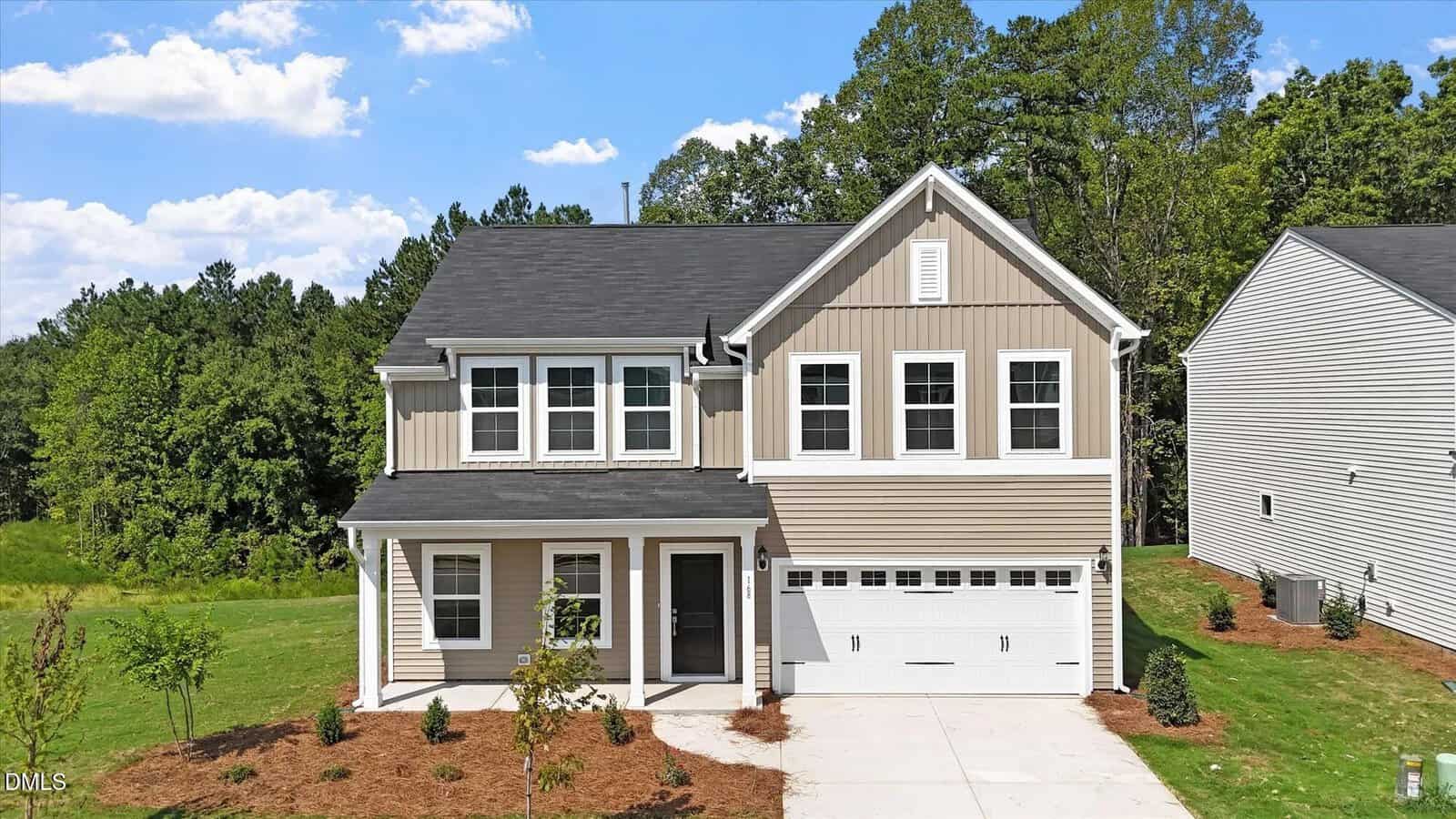 This two-story beige house with white trim at 168 Sugarmaple Way, Youngsville, features a covered front porch and a double garage. The landscaped yard boasts young trees and grass, while the home is bordered by mature trees and neighboring residences.