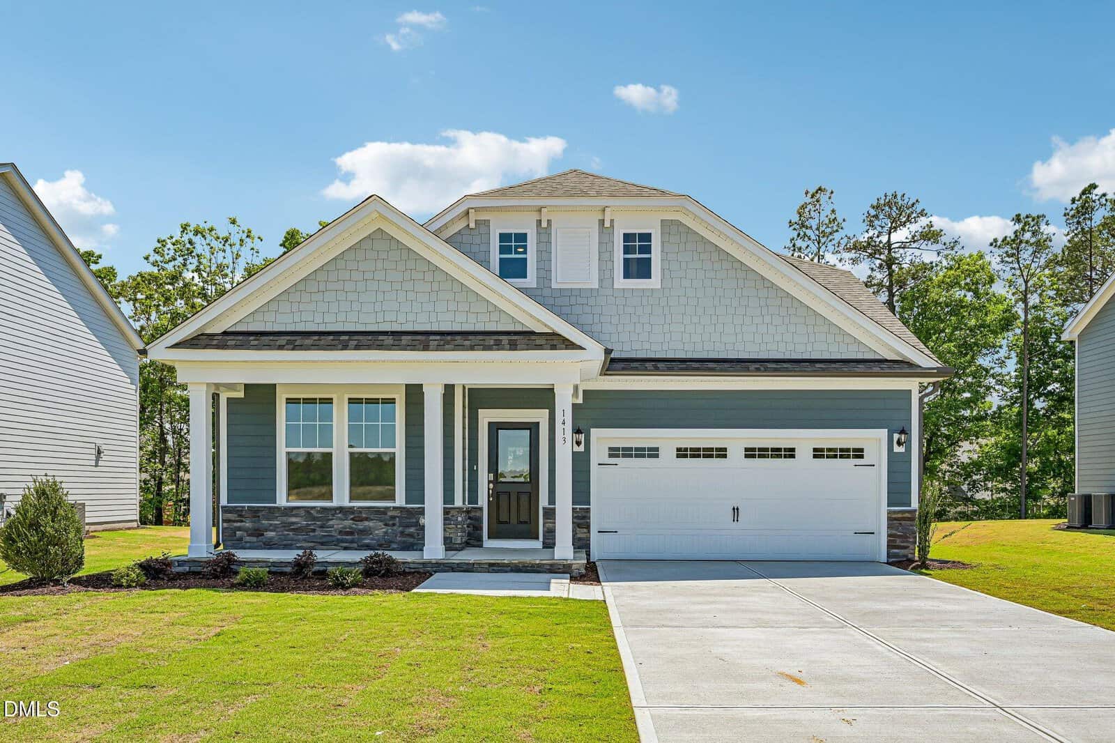 A modern two-story house with gray siding, white trim, a covered front porch, and a double garage, set on a neatly landscaped lawn under a blue sky with scattered clouds.