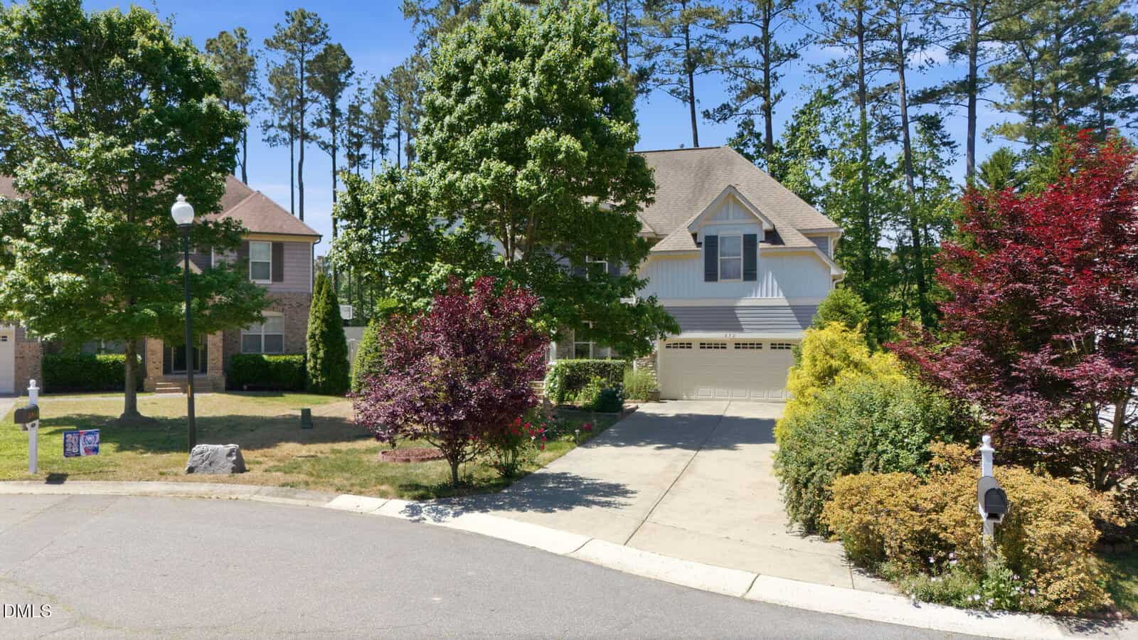 Two suburban houses with sloped roofs, surrounded by green trees and bushes. One house has a driveway leading to a garage, and both houses are located at the end of a quiet cul-de-sac.