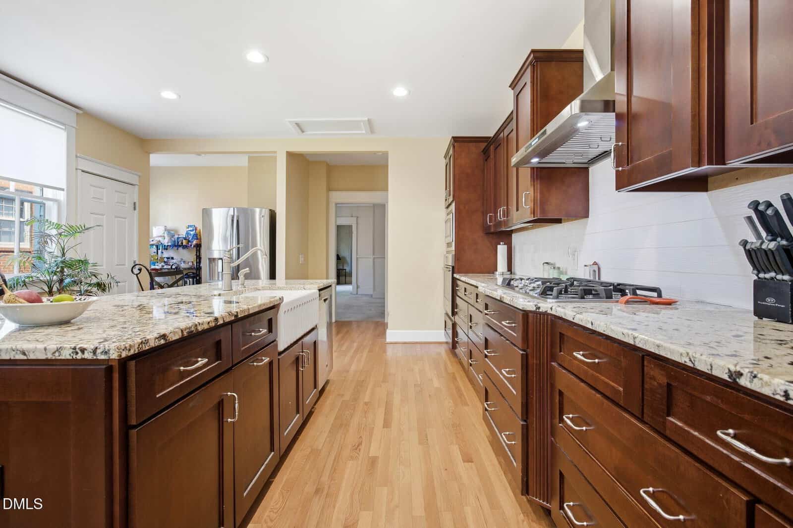 Modern kitchen with dark wood cabinets, granite countertops, a center island, gas stove, knife block, and hardwood floors. Stainless steel appliances and bright lighting create an inviting, functional space.
