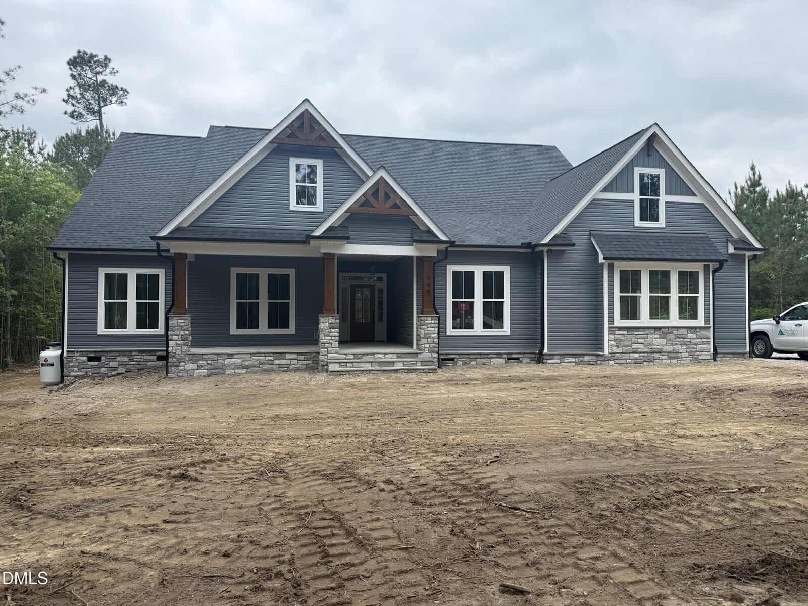 A modern, single-story house at 440 Pilot Ridge Road, Zebulon, features blue-gray siding, stone accents, white trim, a covered porch, gabled roof, and large windows, set on a dirt yard with trees in the background.