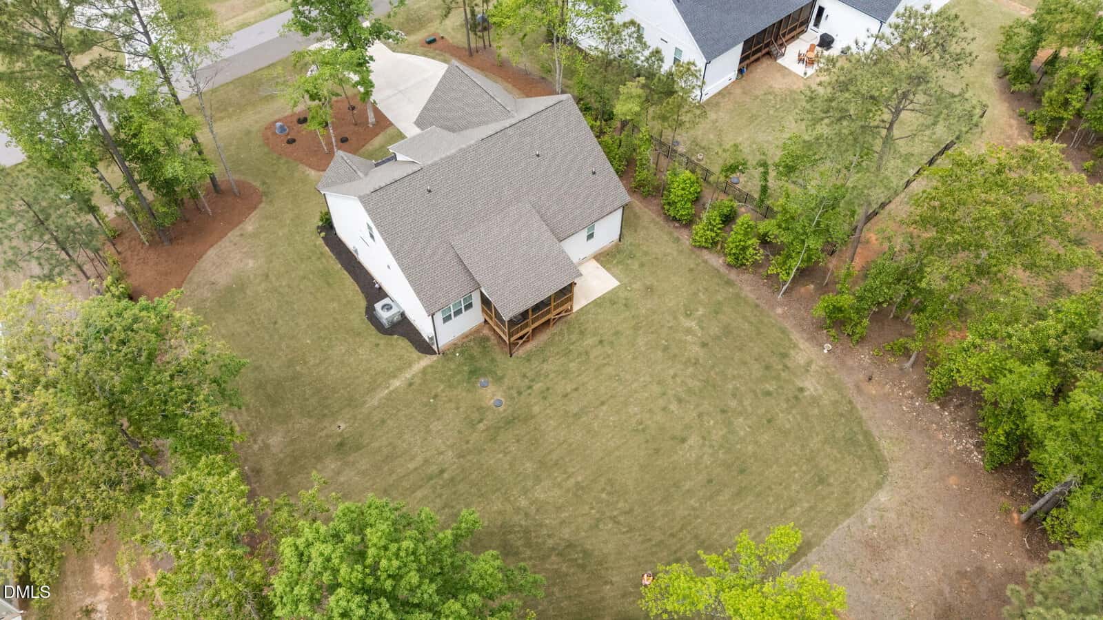 Aerial view of a white house with a gray roof, screened porch, and large, neatly mowed backyard surrounded by trees and neighboring homes.