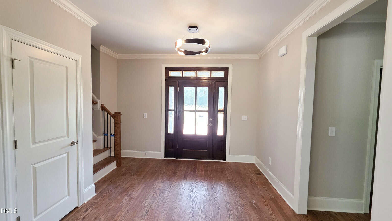 Bright entryway with hardwood floors, a dark wood front door with glass panels, a modern ceiling light, beige walls, white trim, and a staircase on the left.