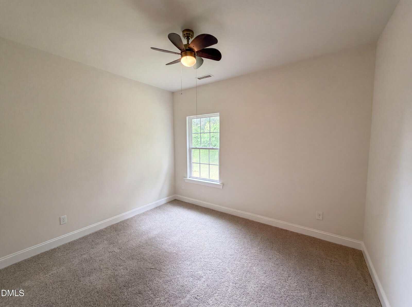 Empty room with beige carpet, white walls, a ceiling fan with lights, and a single window allowing natural light in.