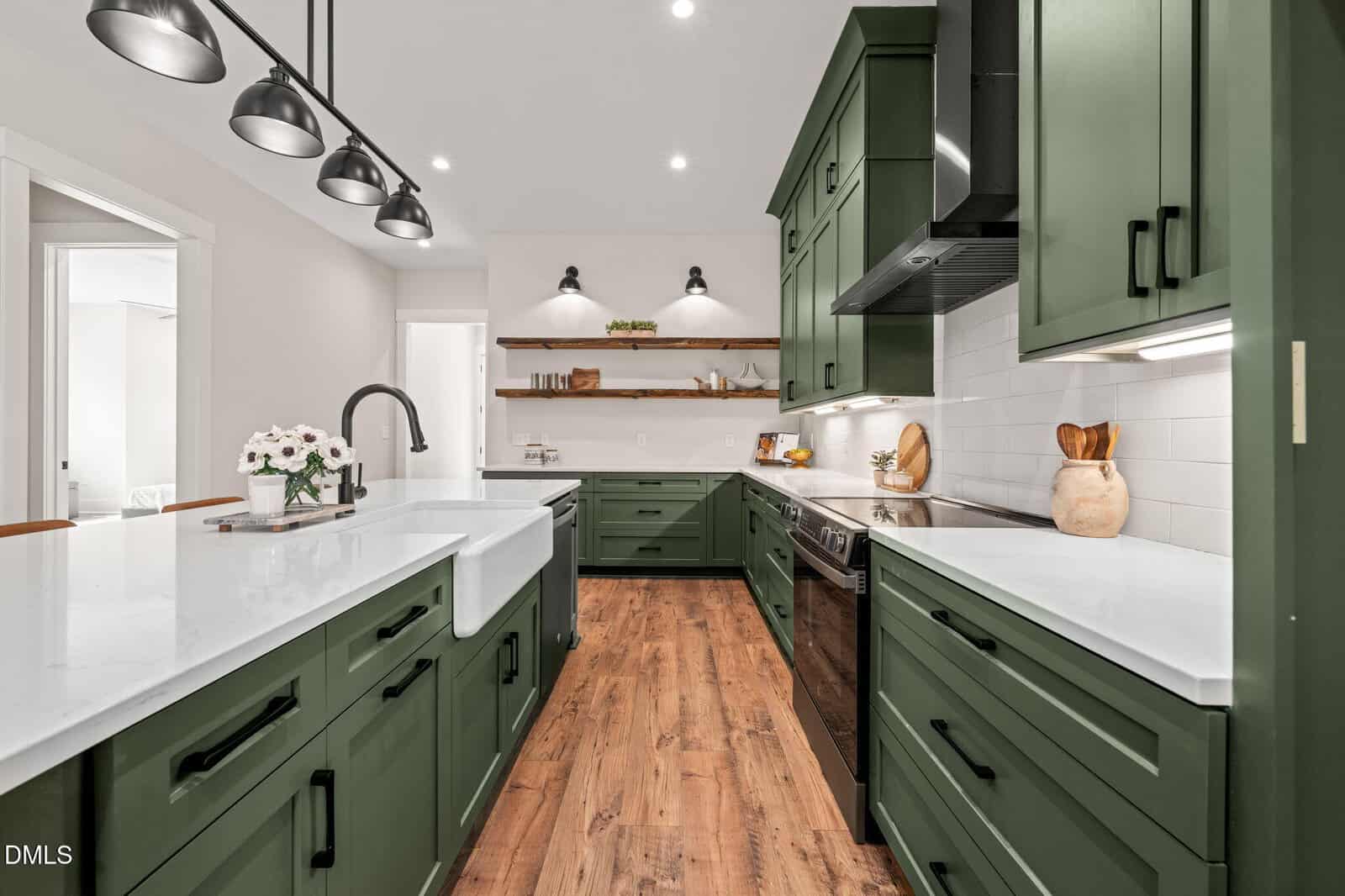 Modern kitchen at 400 Pilot Ridge Road in Zebulon with green cabinets, white countertops, farmhouse sink, stainless steel appliances, white subway tile backsplash, wood floors, and open shelves with decor, under black pendant and wall lighting.