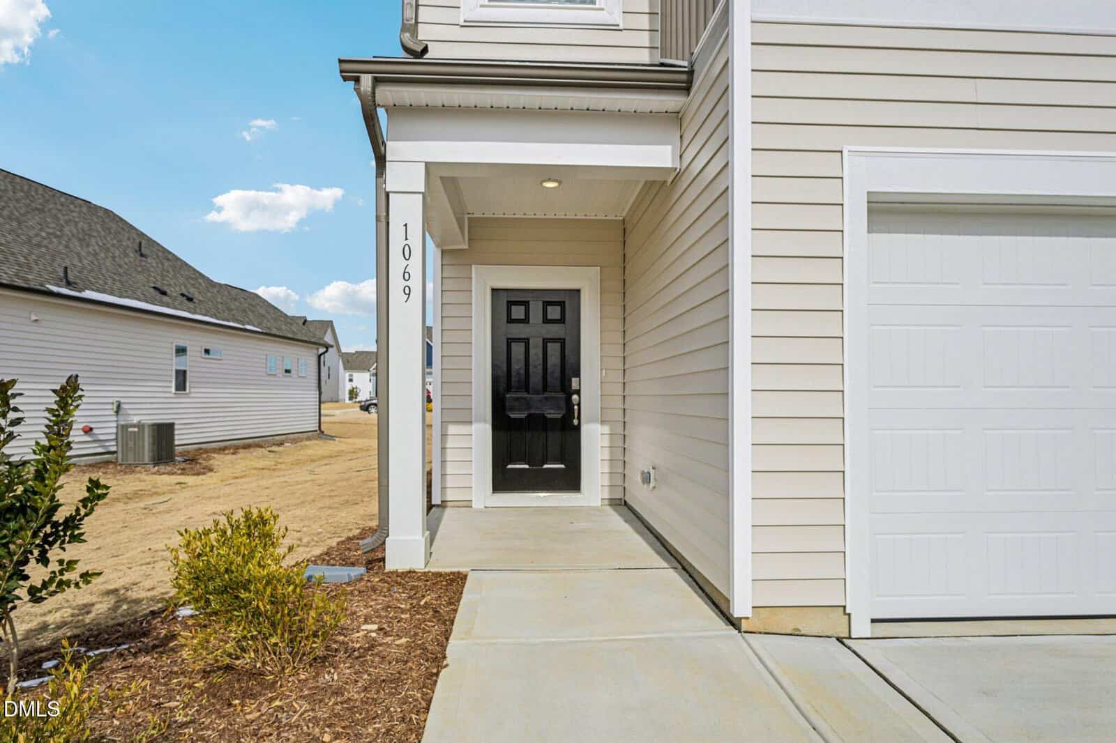 A modern beige house in Franklinton with a black front door, white trim, and a covered entryway. The house number 1069 is visible on a post, with small bushes along the walkway. Other homes line 39 Gerrard Street in the background.