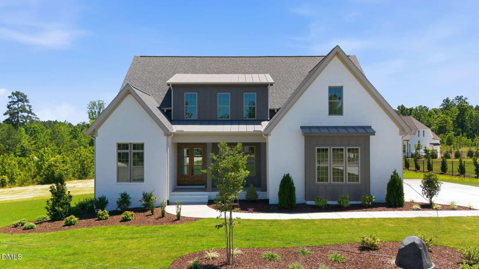 A modern two-story white house with gray accents at 30 Serenity Woods Trail, Franklinton, features large front windows, a covered porch, and a neatly landscaped yard with young trees and shrubs on a sunny day.