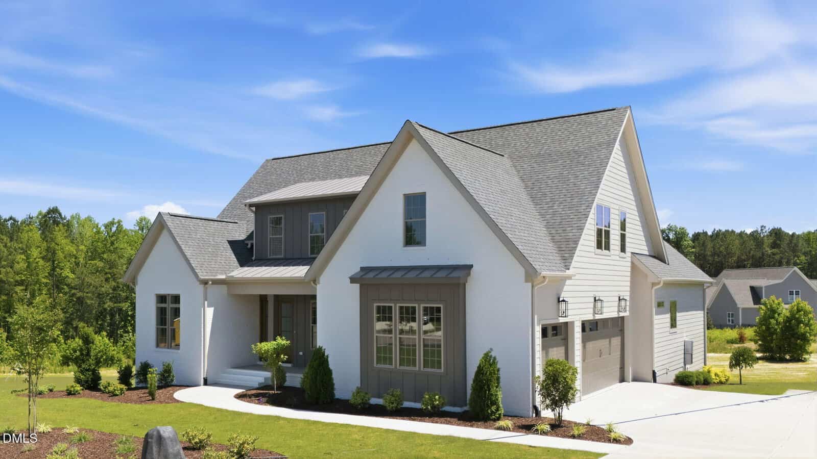 A modern two-story white house with gray roof and trim, large windows, and a double garage, surrounded by a manicured lawn and shrubs, set against a backdrop of trees under a blue sky.