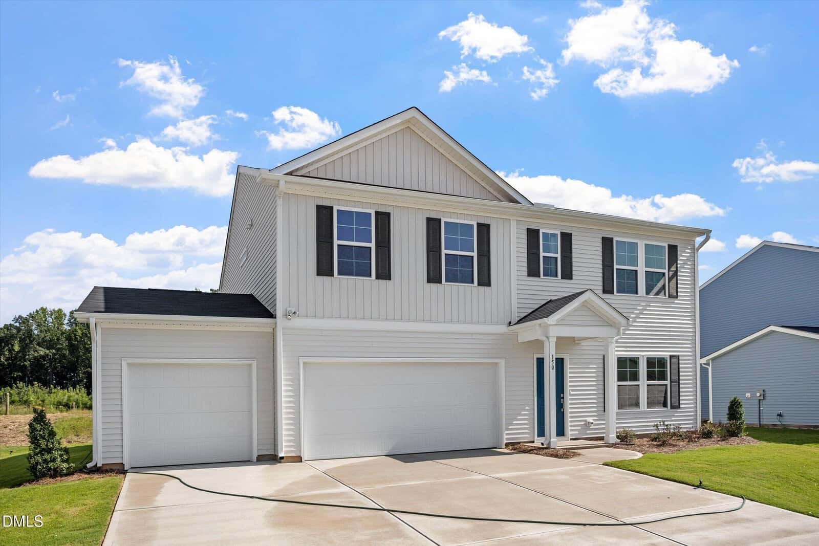 Two-story white house with black shutters, double garage, and blue front door. The driveway is wide and curved, with a small lawn and clear blue sky in the background.