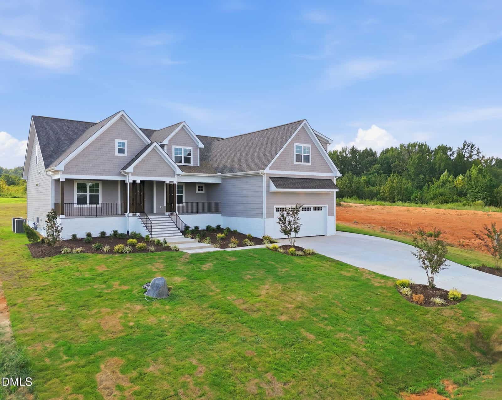 A modern gray house with white trim, front porch, attached two-car garage, and neatly landscaped lawn, set against a backdrop of trees and a blue sky.