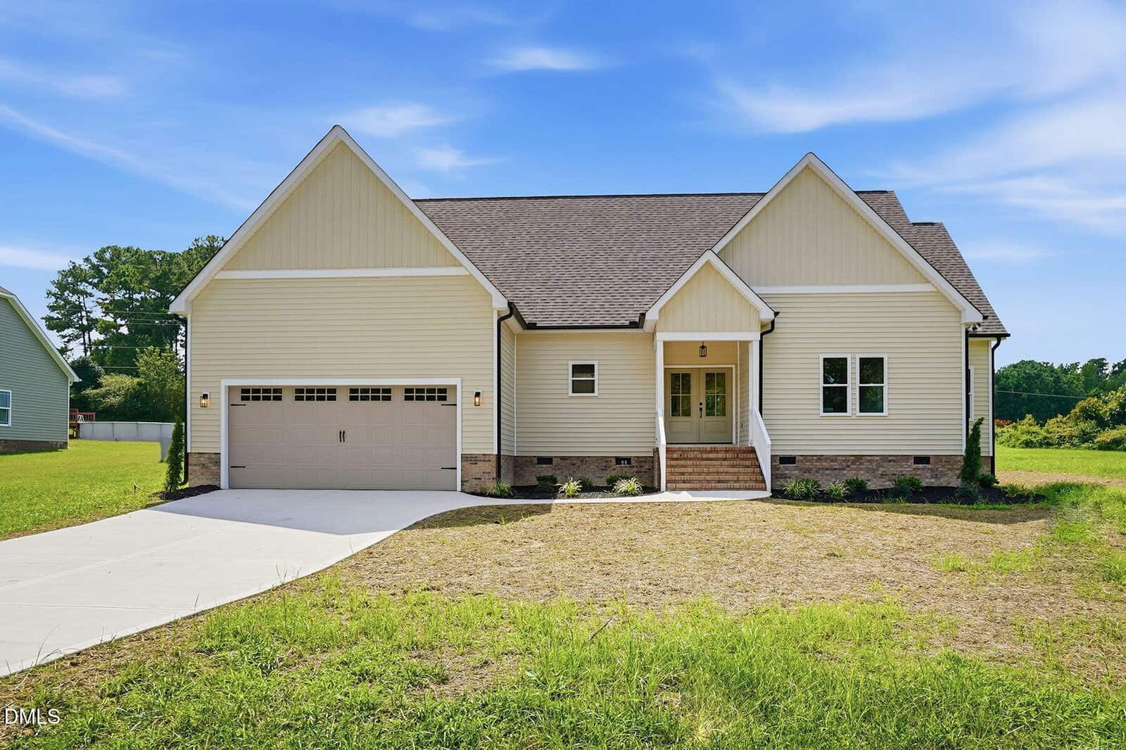 Single-story beige house with a dark shingle roof, attached two-car garage, front steps leading to a covered entry, and a concrete driveway. Nestled on 35 Cotton Drive in Louisburg, the home features a grass yard surrounding the property with trees in the background under a clear blue sky.
