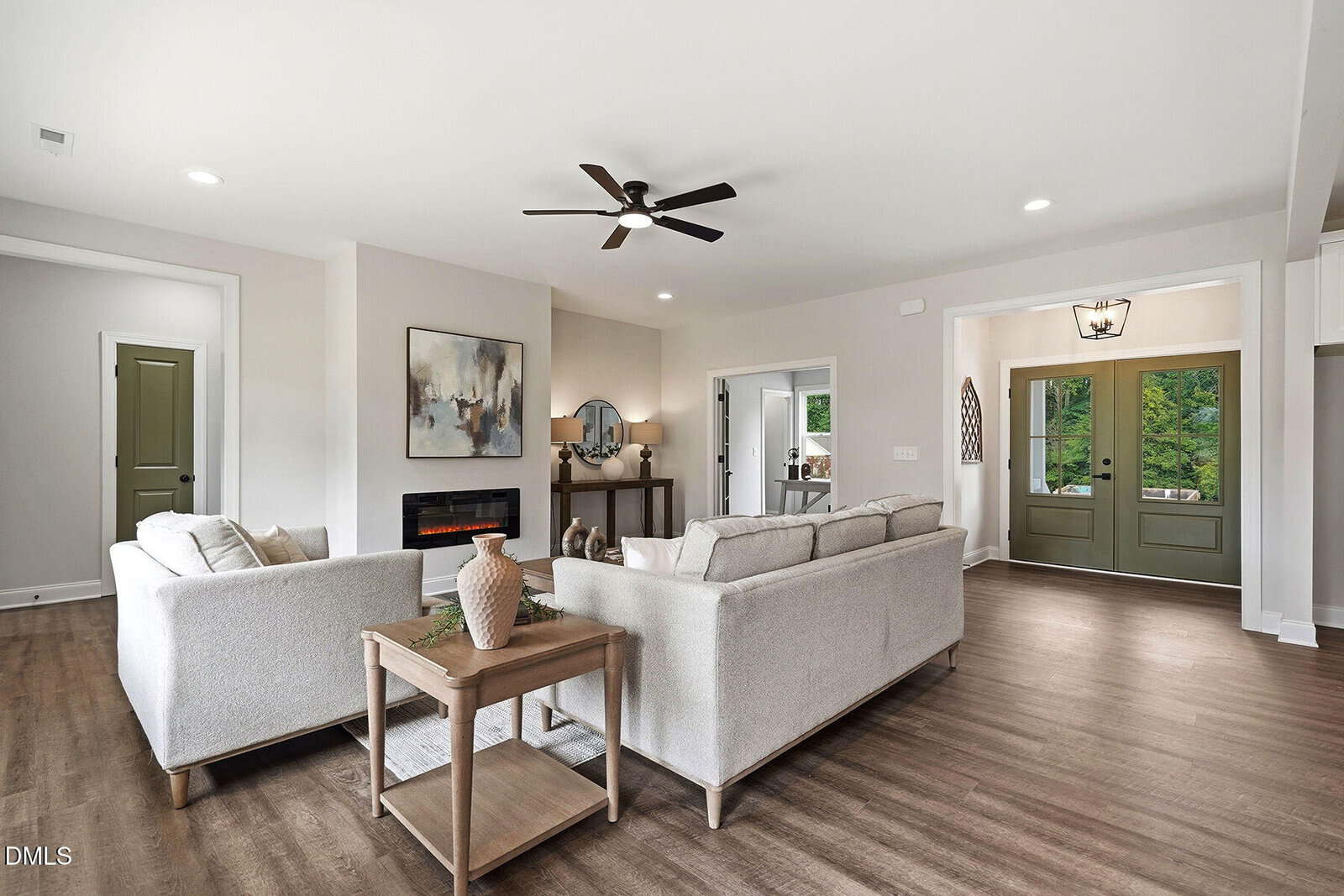 Modern living room with two beige sofas, wooden table, decor accents, and wood flooring. Green double doors and natural light brighten the open space. Neutral, minimalist style throughout.