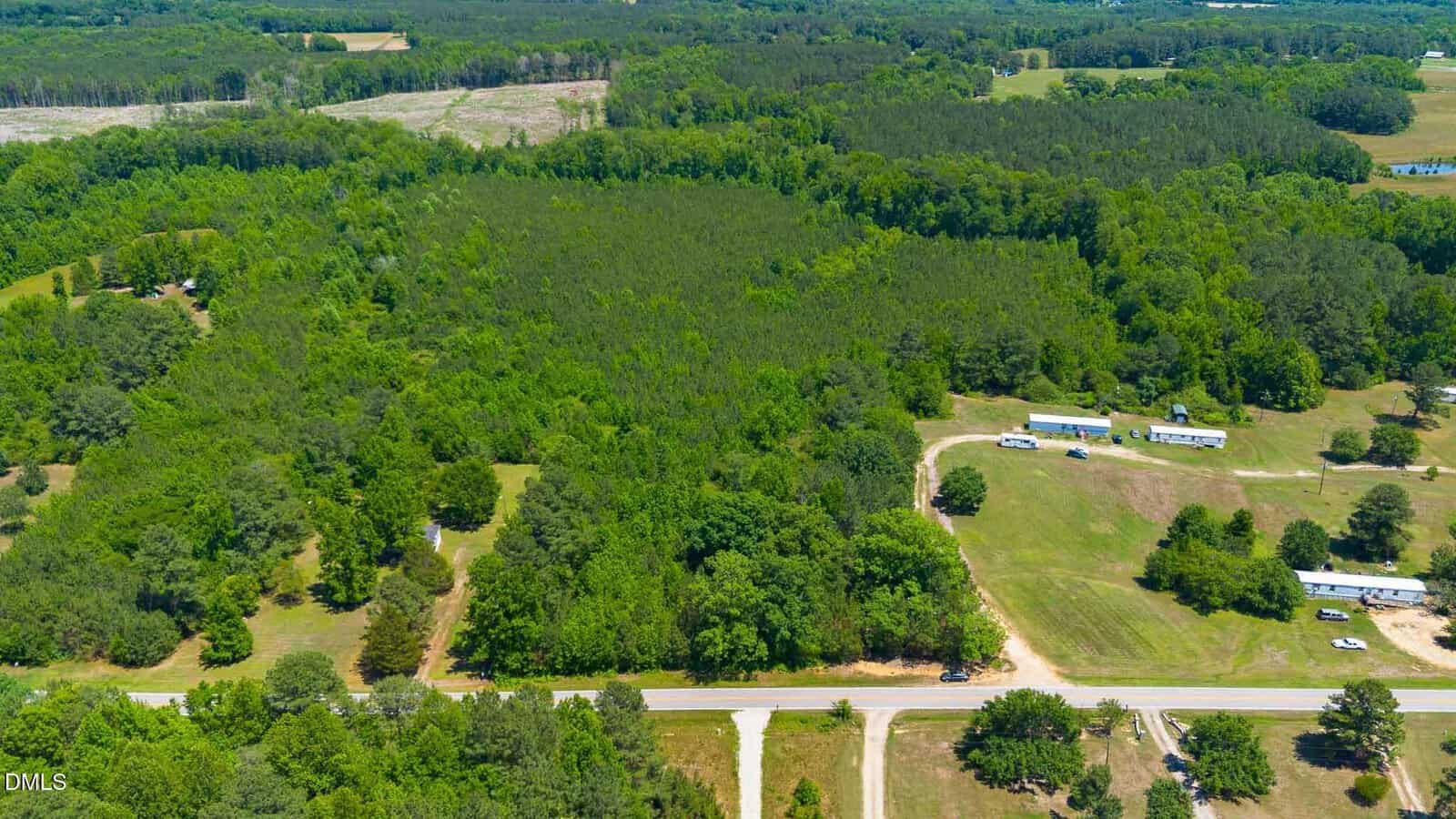 Aerial view of a rural, forested area near 0000 Laurel Mill Road, Louisburg, with a main road running horizontally, scattered houses along driveways, open grassy fields, and dense green trees stretching into the distance.