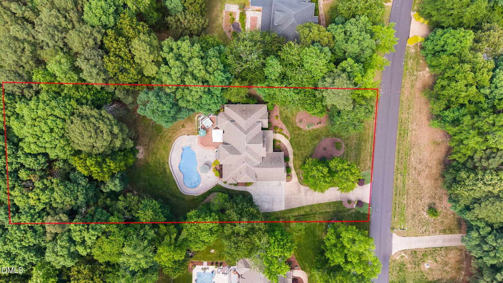 Aerial view of a house with a swimming pool, driveway, and surrounding trees. The property is outlined in red, showing its boundaries, and is adjacent to a road and neighboring homes.