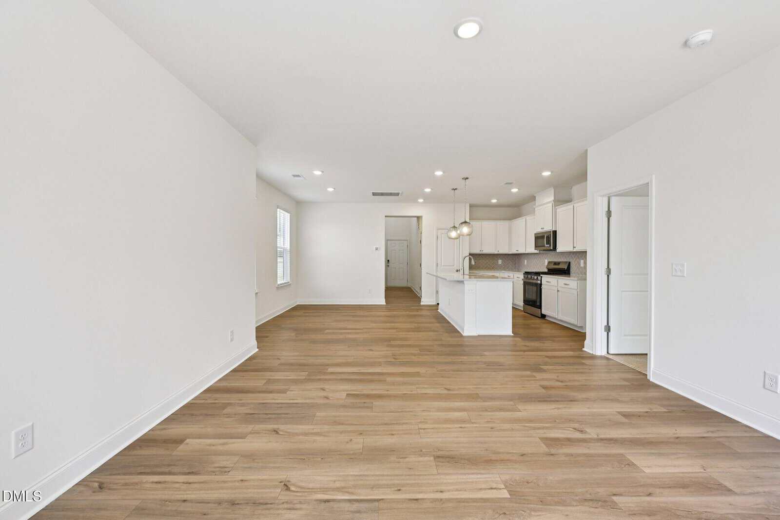 A spacious, bright, open-concept living area and kitchen with white walls, light wood flooring, and a white island.