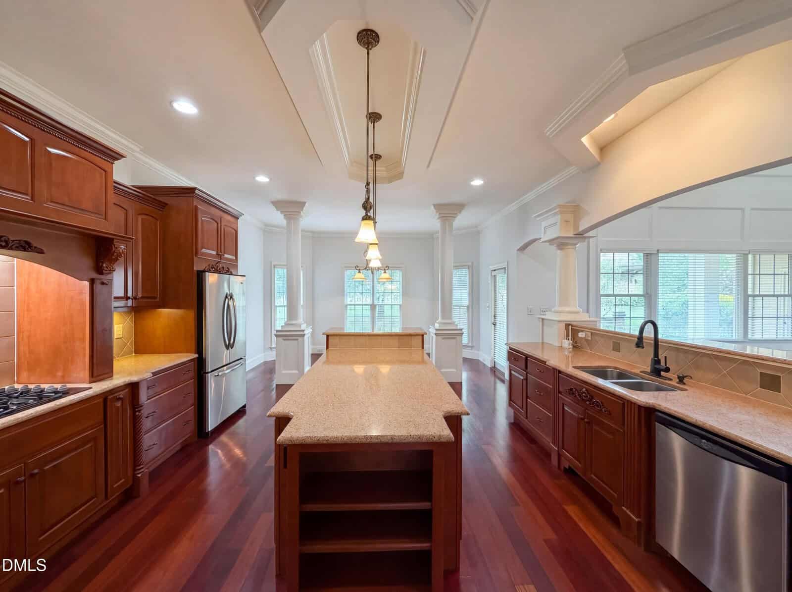 Spacious kitchen with dark wood cabinets, stainless steel appliances, a center island, pendant lighting, and large windows letting in natural light onto polished hardwood floors.