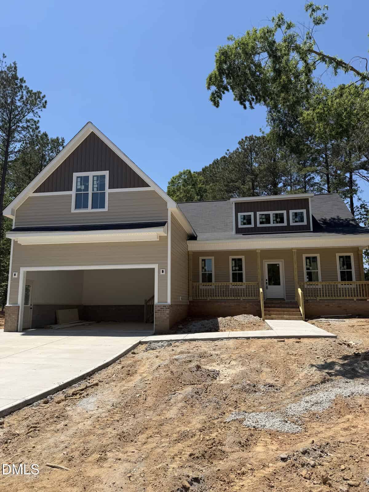 A newly constructed two-story house at 75 Copper Penny Road, Zebulon, with beige siding, a large front porch, double garage, and a steep driveway on a dirt yard, surrounded by tall trees under a clear blue sky.