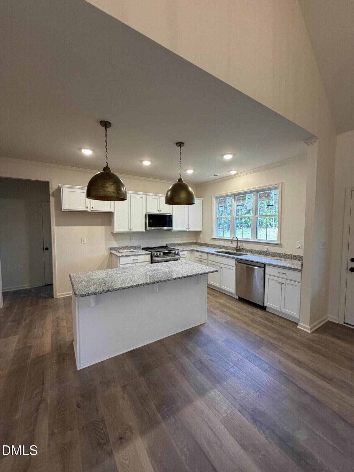 Modern kitchen with white cabinets, granite countertops, stainless steel appliances, two large pendant lights, and wood flooring. Large windows above the sink let in natural light. Open layout with an island in the center.