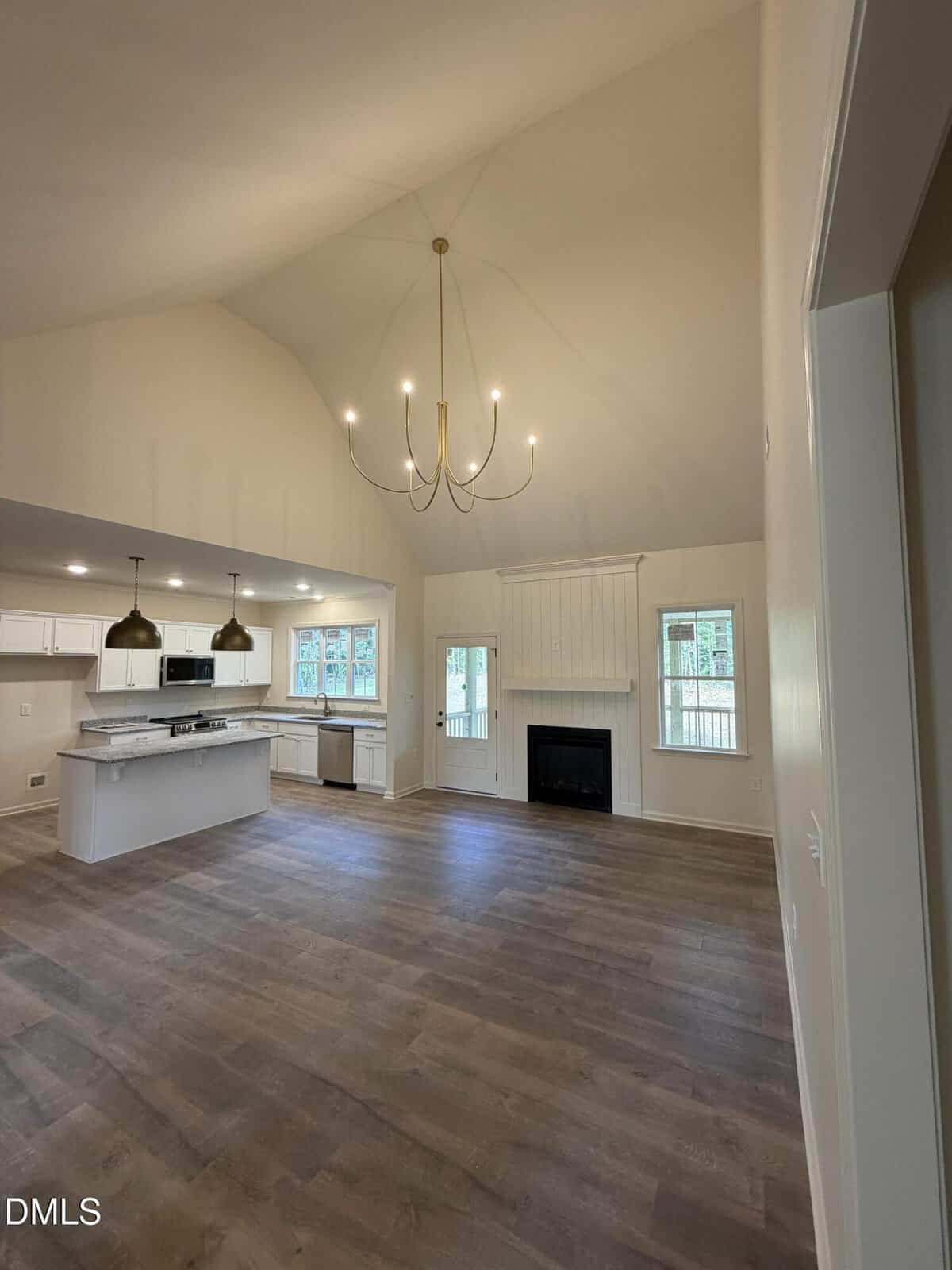 Open-concept kitchen and living room with wood floors, modern light fixtures, white cabinets, a central island, fireplace, and large windows letting in natural light.