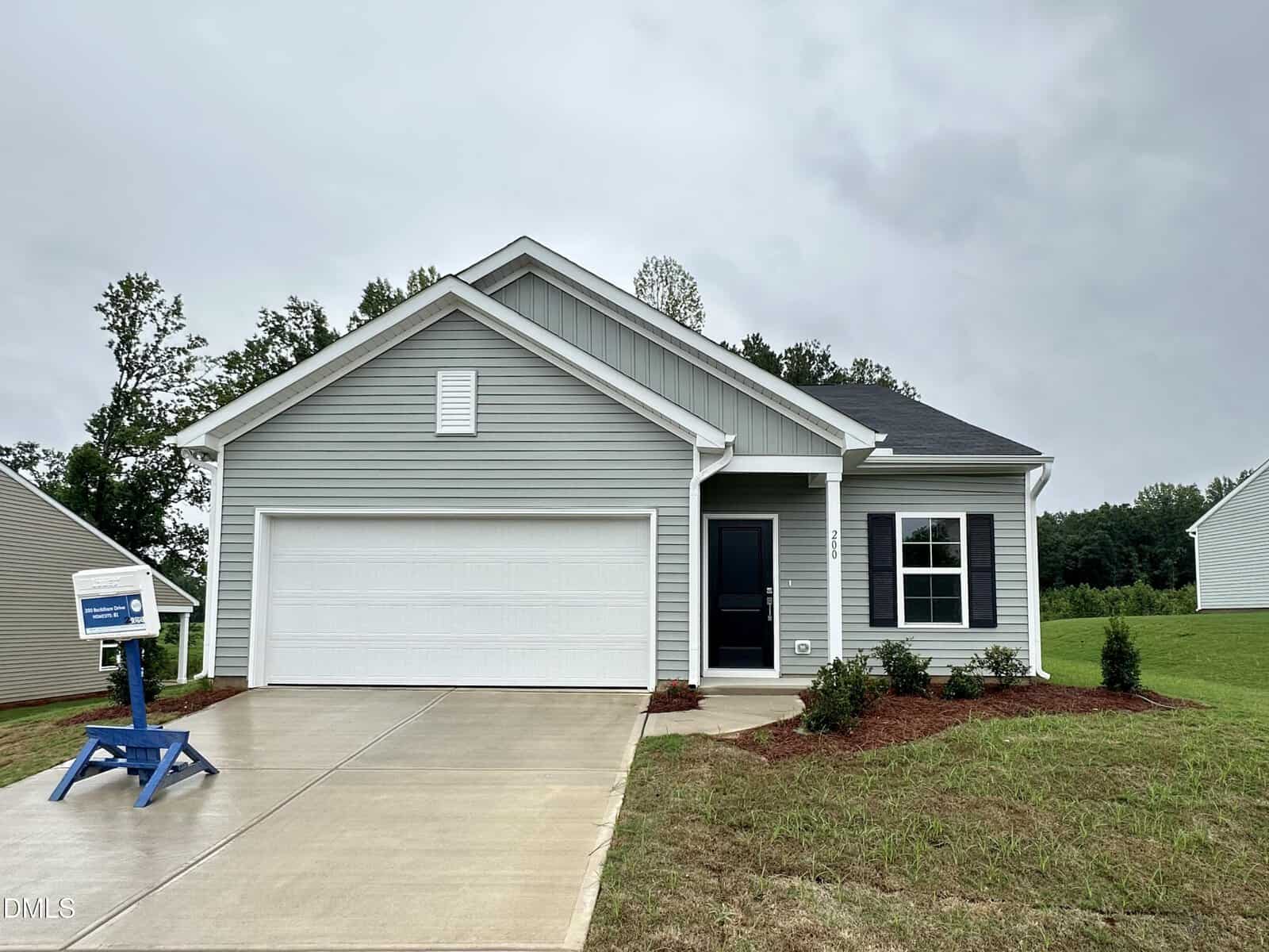 Single-story house with light gray siding, white trim, and a front-facing garage situated at 200 Buckthorn Drive in Youngsville. Concrete driveway leads to the garage. Grass lawn with sparse landscaping surrounds the house. Sky is overcast.