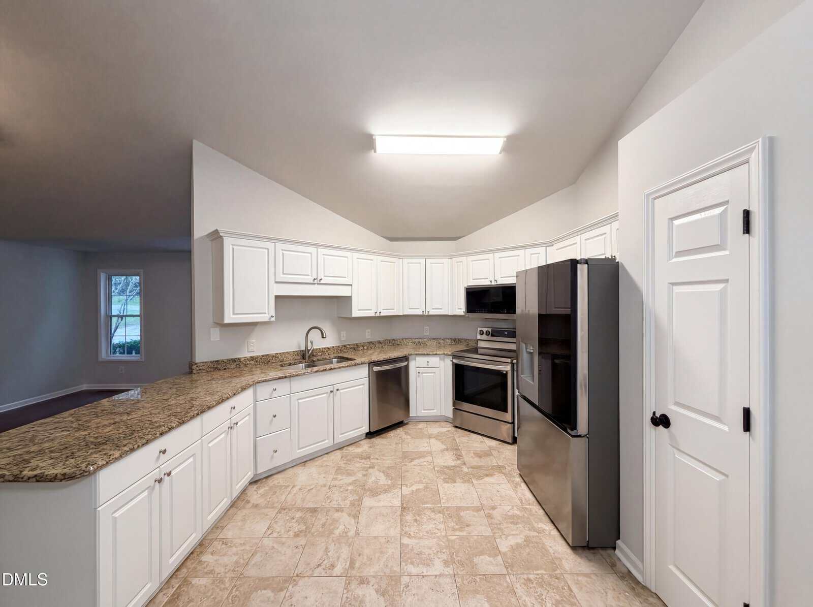 Modern kitchen with white cabinets, stainless steel appliances, granite countertops, and beige tile floor. An adjacent room with a window is visible, and the ceiling has recessed lighting. A white door is on the right wall.