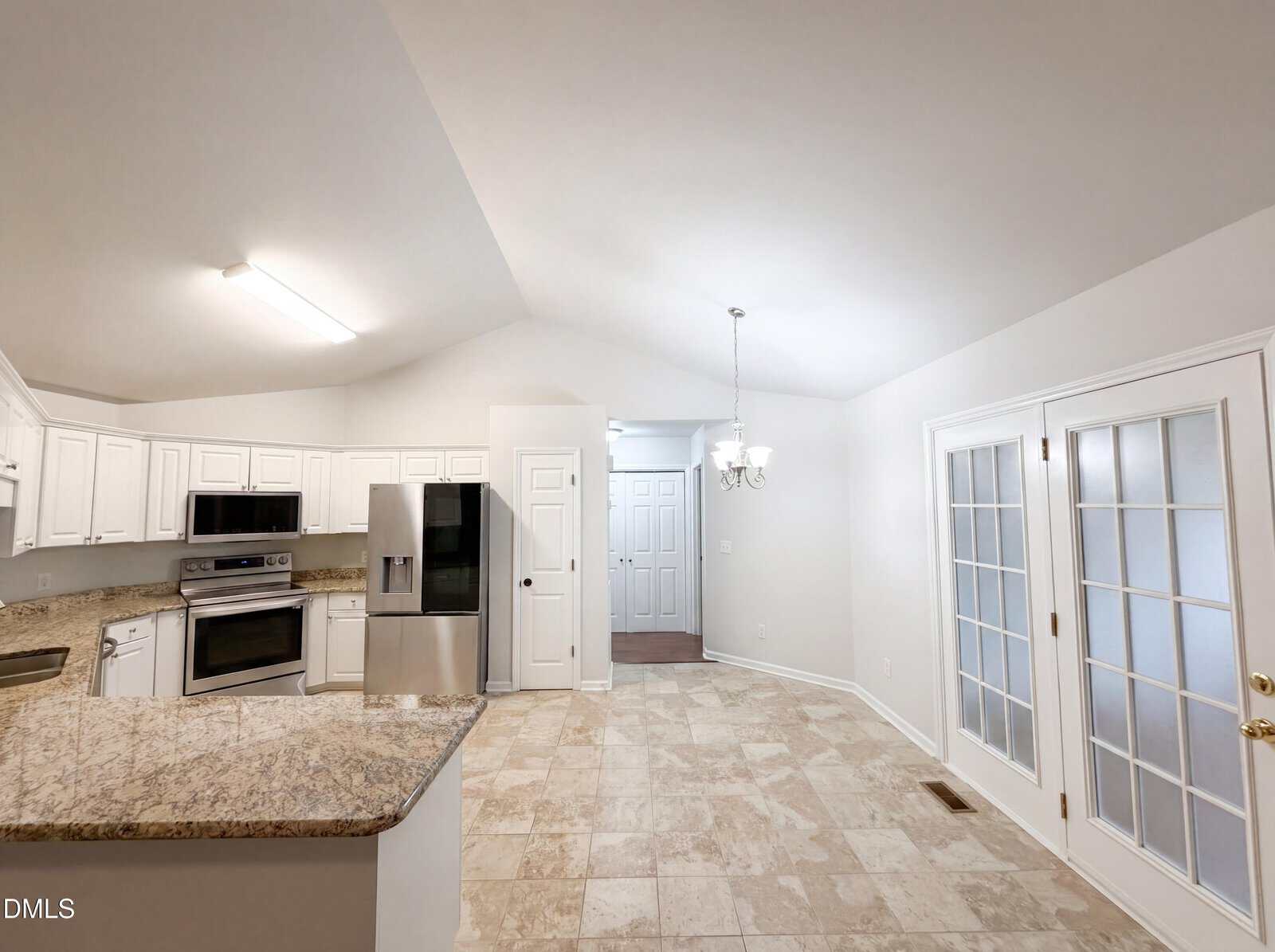 Spacious kitchen with light tile flooring, white cabinets, granite countertops, stainless steel appliances, and recessed lighting. Glass doors and a chandelier are visible, as well as a hallway and closed doors in the background.